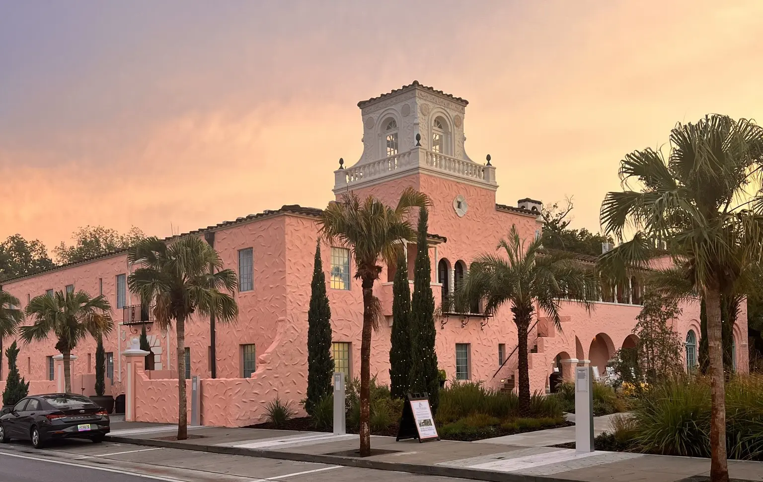 The Hacienda Hotel’s pink facade and tower beneath a sunset sky, with palm trees along the entrance.